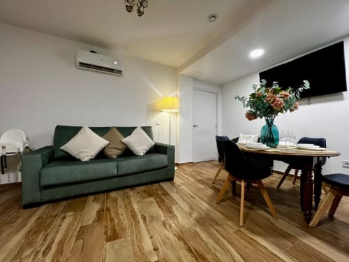 Apartamento moderno en Las Arenas Valencia con sofá verde, mesa de comedor, suelos de madera y TV de pantalla plana
