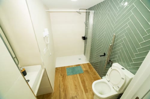 Baño moderno en apartamento Las Arenas con azulejos verde espiga, suelos de madera y accesorios blancos en Valencia