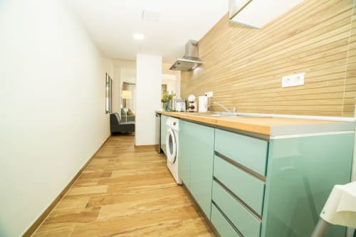 Cocina moderna con muebles verde menta, revestimiento de madera y lavadora en el apartamento Las Arenas de Valencia