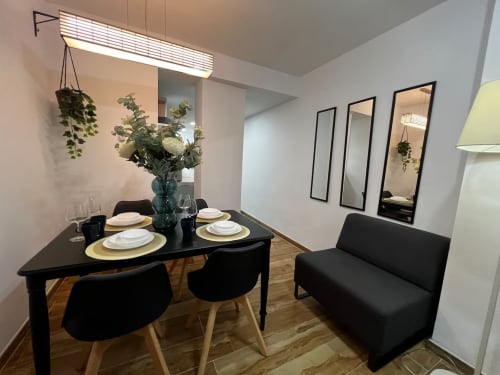 Comedor del apartamento Las Arenas Valencia con mesa negra, sillas modernas, vajilla y arreglo floral