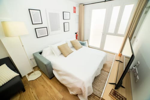Dormitorio luminoso y moderno en apartamento Las Arenas de Valencia con ropa de cama blanca, suelos de madera y amplias ventanas con vistas