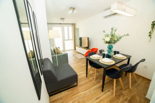 Elegante comedor en apartamento Las Arenas Valencia con mesa negra, vajilla blanca, flores frescas y salón integrado