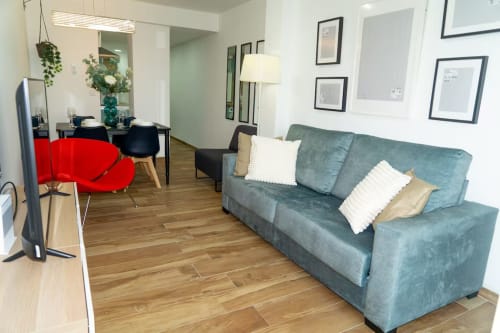 Moderna sala de estar del apartamento Las Arenas Valencia con sofá turquesa, silla roja y piso de madera