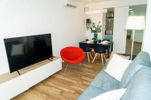 Sala de estar del apartamento Las Arenas con sofá gris, silla roja, televisor y comedor en Valencia