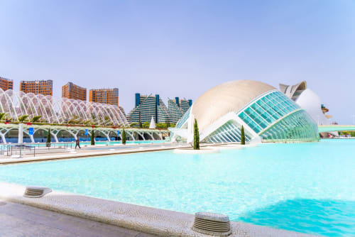 Frente de playa Las Arenas Valencia con piscina turquesa, domo arquitectónico blanco y edificios modernos bajo cielo azul
