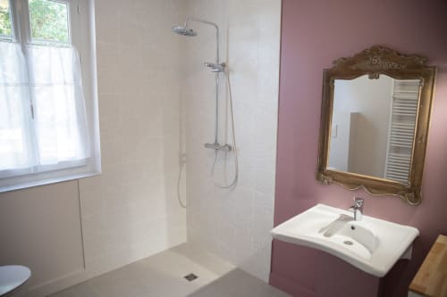 Salle de bain accessible moderne au Domaine de Castagnère avec douche italienne, lavabo blanc, miroir orné et mur d'accent rose