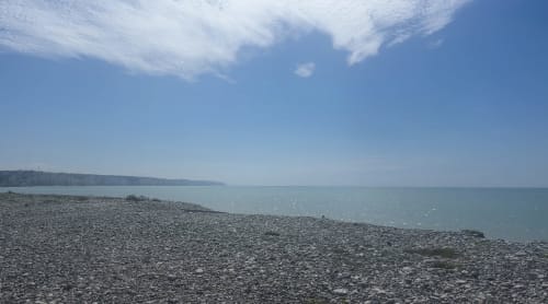 Plage de galets à l'hôtel Hidden Bay à Cayeux-sur-Mer, avec une mer turquoise calme et des nuages blancs