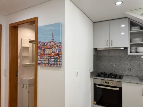 Modern kitchen in Chaves apartment with white cabinets, gas stove, and Porto-themed wall art