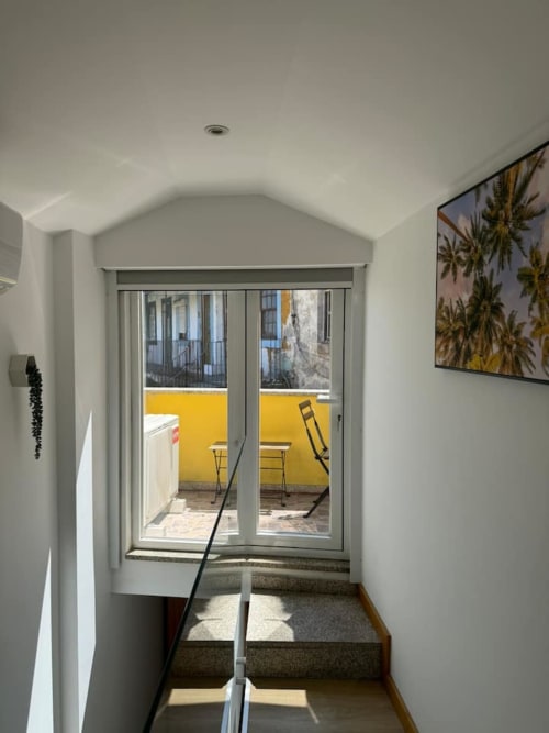 Bright stairwell leading to yellow-walled balcony with palm tree view at Voluta Management apartment in Chaves, Portugal