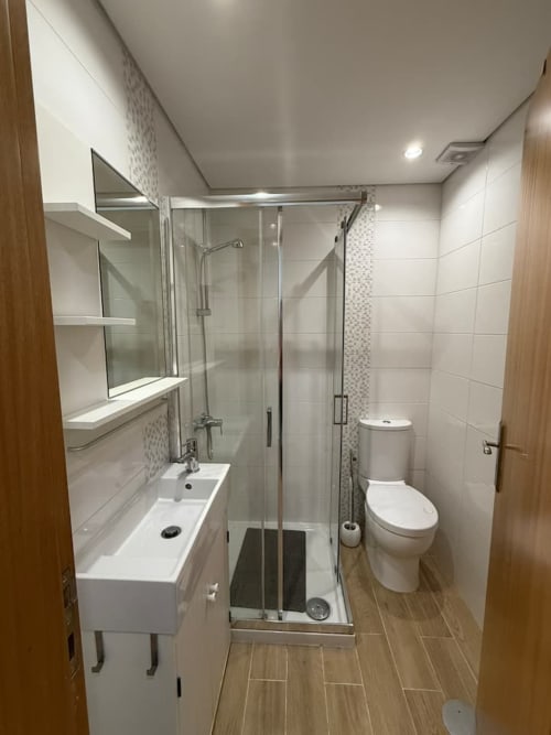 Modern bathroom with glass shower enclosure, white sink vanity, and toilet in Chaves apartment rental