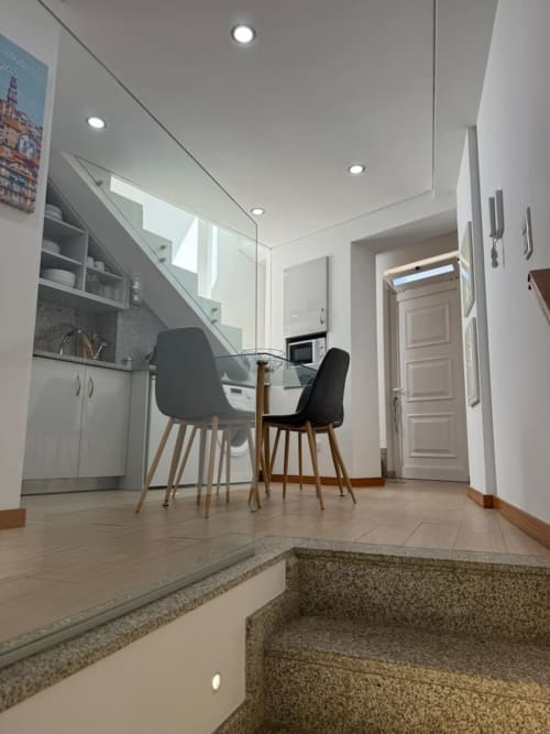 Modern apartment kitchen and dining area in Chaves with glass staircase, white cabinetry, and black chairs at table