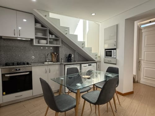 Modern kitchen and dining area in Chaves apartment with glass table, black chairs, white cabinets, and staircase