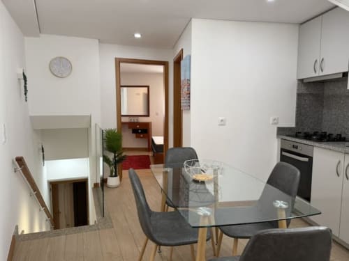 Modern kitchen-dining area in Chaves apartment with glass table, dark chairs, white cabinetry, and wooden floors