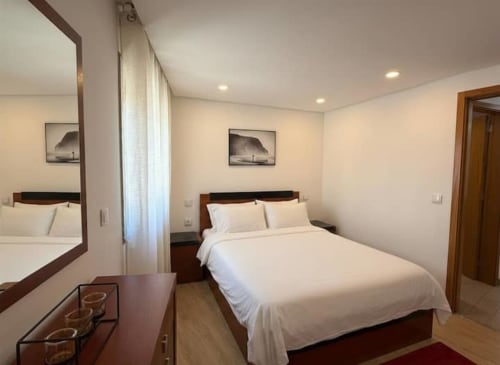 Modern bedroom with white bedding, wooden furniture, and mirror at Voluta Management apartment in Chaves