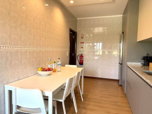 Modern kitchen and dining area in Chaves apartment with white table, chairs, tiled walls, and wooden flooring