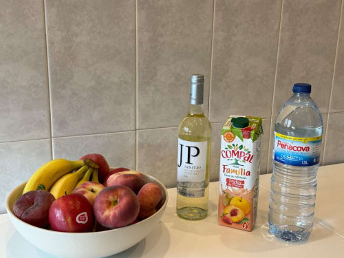 Welcome amenities in Chaves apartment: fresh fruit bowl, white wine, juice, and water bottle on kitchen counter