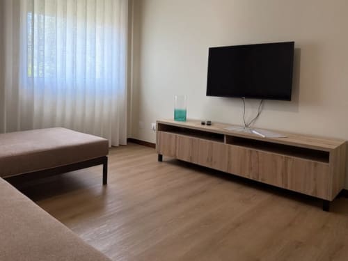 Modern apartment living room in Chaves with flat-screen TV, wooden furniture, and natural light from sheer curtains