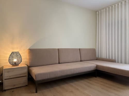 Modern L-shaped gray sofa with wooden side table and woven lamp in bright apartment, Chaves Portugal