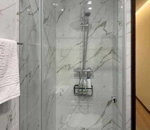 Modern marble shower enclosure with rainfall showerhead and storage caddy in Chaves apartment