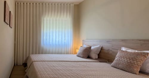 Cozy bedroom with twin beds, striped bedding, decorative pillows, wooden headboard, and sheer curtains at Voluta Management