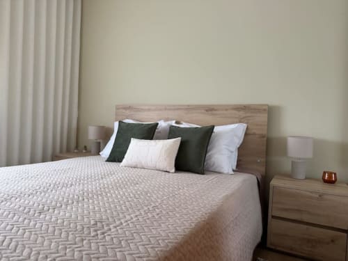 Modern bedroom with wooden headboard, green and white pillows, neutral bedding, nightstands, and flowing curtains at Voluta