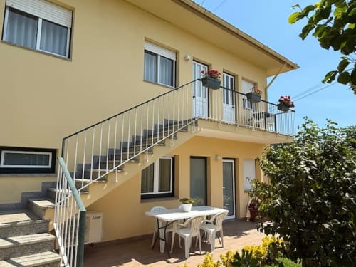 Yellow apartment with terrace staircase, white railing, and ground-level patio with table in Chaves, Portugal