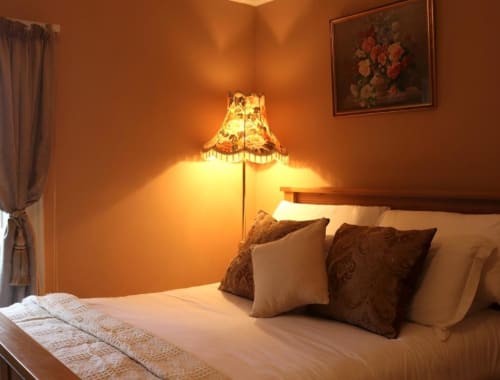 Chambre cosy de la maison d'hôtes South Hill avec murs orange chaleureux, lampadaire allumé et coussins décoratifs sur le lit