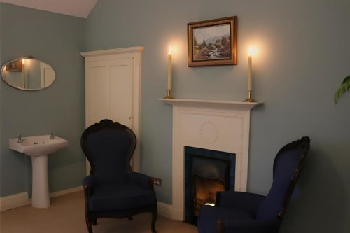 Élégant séjour du cottage South Hill House avec cheminée, deux fauteuils bleu marine, manteau blanc et vue sur le jardin