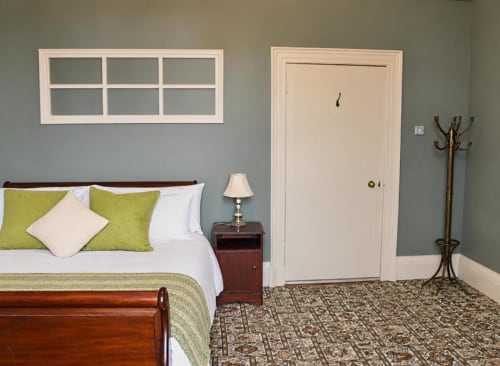 Chambre du gîte South Hill House à Delvin avec lit en bois, oreillers vert citron, lampe de chevet, porte crème et