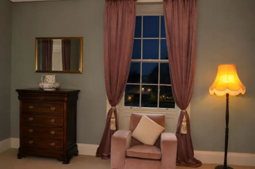 Coin salon élégant de South Hill House avec fauteuil lie-de-vin, miroir ornementé, commode en bois et vue sur le jardin