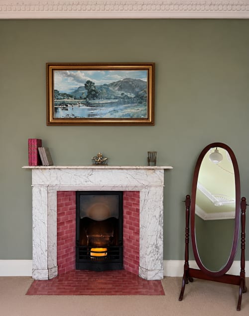 Élégante cheminée de la suite prestige de South Hill House, encadrement en marbre, intérieur en briques rouges, tableau de paysage orné au-dessus.