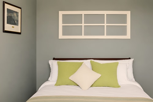 Chambre à South Hill House, Delvin avec lit, oreillers vert citron, literie crème et cadre de fenêtre décoratif au-dessus.