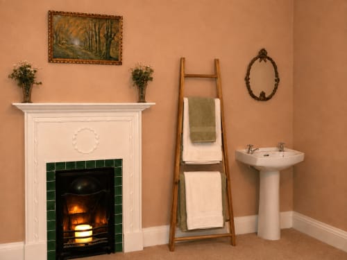Élégante cheminée de South Hill House à Delvin : manteau blanc, foyer aux carreaux verts, sèche-serviettes en bois, colonne