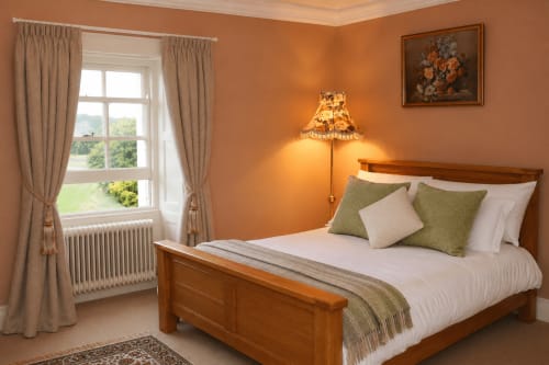 Chambre chaleureuse aux tons d'orange à South Hill House, Delvin, avec lit en bois, coussins verts et vue sur le jardin depuis la baie vitrée