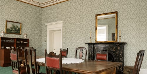 Élégante salle à manger de South Hill House avec table en bois, cheminée, papier peint damassé et miroir à cadre doré