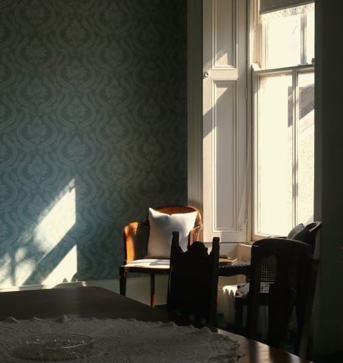 Chambre ensoleillée de South Hill House avec papier peint à motifs damassés, chaise en rotin, coussin blanc et vue sur le jardin à Delvin.