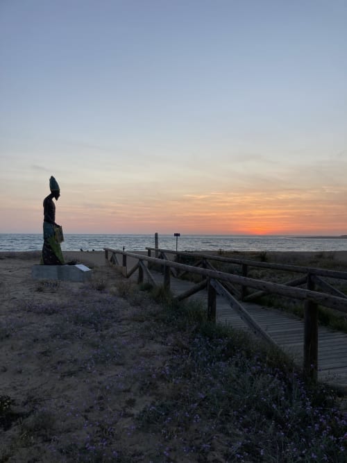 Vista de playa al atardecer en G&H Apartments, Jerez de la Frontera, con pasarela de madera y escultura de dunas