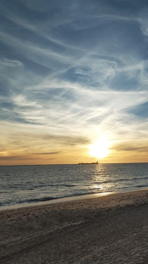Vista de playa al atardecer con luz dorada reflejándose en las olas del océano y la orilla arenosa