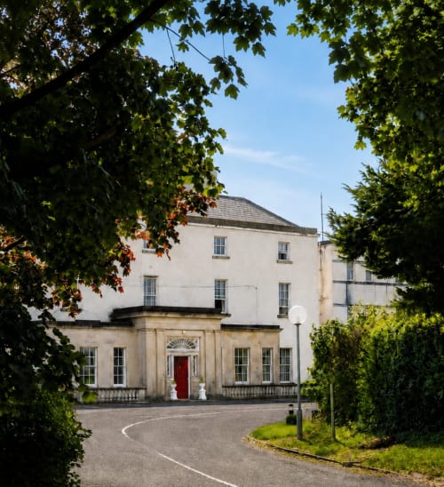 Entrée de l'hôtel South Hill House à Delvin, Irlande, façade en pierre avec porte rouge entourée de végétation verte luxuriante