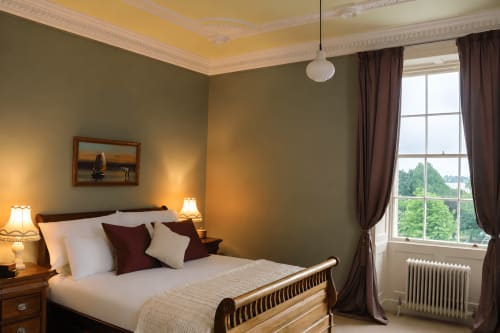 Chambre élégante de South Hill House à Delvin avec plafond jaune, murs olive, lit en bois, luminaire suspendu et vue sur le jardin