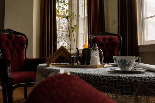 Service à thé élégant à South Hill House avec fauteuils cabriolets bordeaux, fenêtres et mobilier d'époque