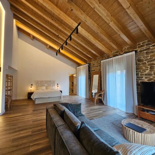 Suite Izarbe con vigas de madera vista, paredes de piedra, cama, sala de estar y comodidades modernas en España