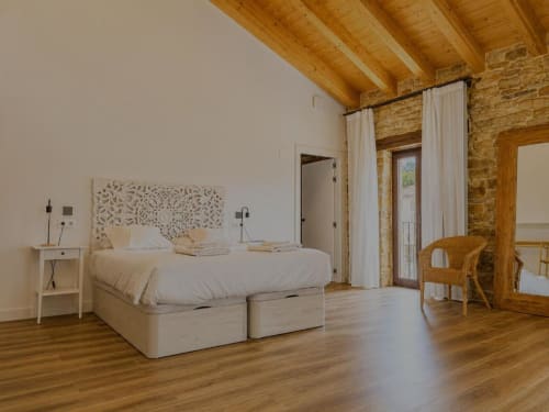 Espaciosa Suite del Hotel Izarbe con vigas de madera, muros de piedra, ropa de cama crema y suelos de madera