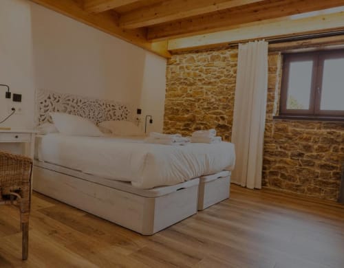 Habitación doble en Hotel Izarbe con ropa de cama blanca, vigas de madera, pared de piedra y suelo de madera