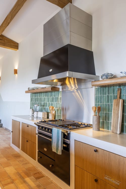 Cuisine moderne de la villa Ersa avec cuisinière noire, hotte inox, placards en bois et dosseret en carrelage vert