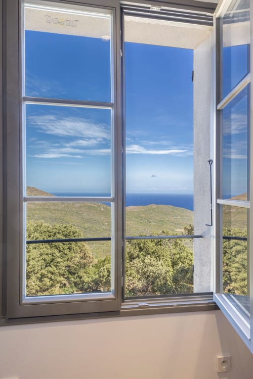 Fenêtre ouverte sur la mer Méditerranée, collines verdoyantes et ciel bleu à la villa La Conciergerie du Cap Corse en Corse