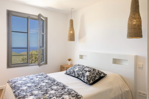 Chambre de la villa Constance à La Conciergerie du Cap Corse avec vue sur mer, luminaires suspendus et literie blanche moderne