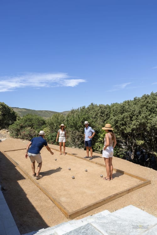 Des clients jouent à la pétanque sur un terrain de sable à la villa La Conciergerie du Cap Corse avec vue sur le jardin en pente