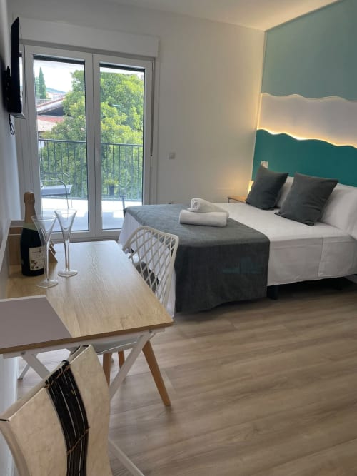 Habitación moderna del Hotel Arenas Rio con cabecero verde, cama blanca, escritorio de madera y balcón con vistas al río