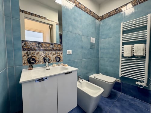 Bagno moderno presso Aurora View Resort con piastrelle turchesi, lavabo bianco, bidet, scaldasalviette e dettagli decorativi